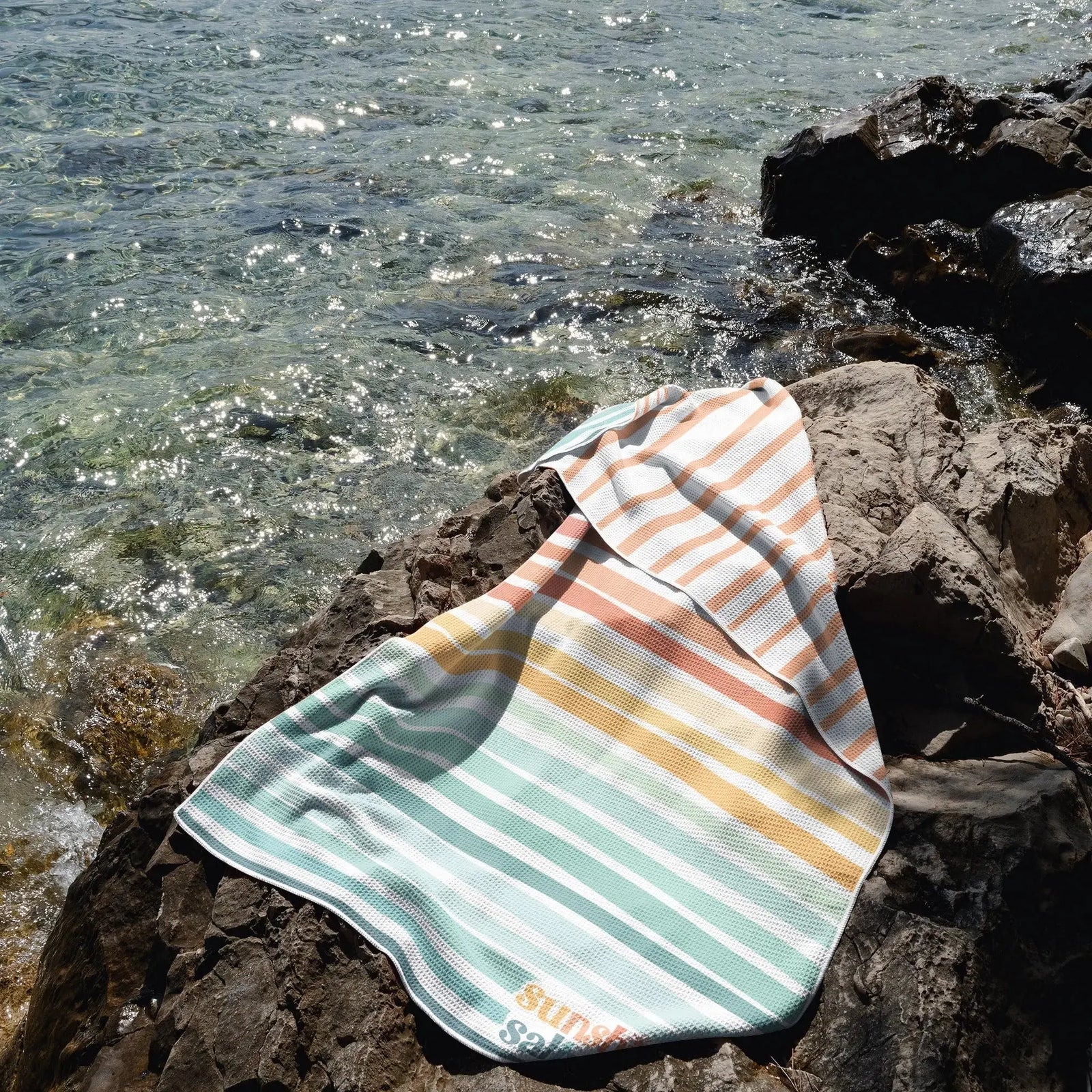 mermaid beach towel in rainbow hues sprawled out on a cliff overlooking ocean