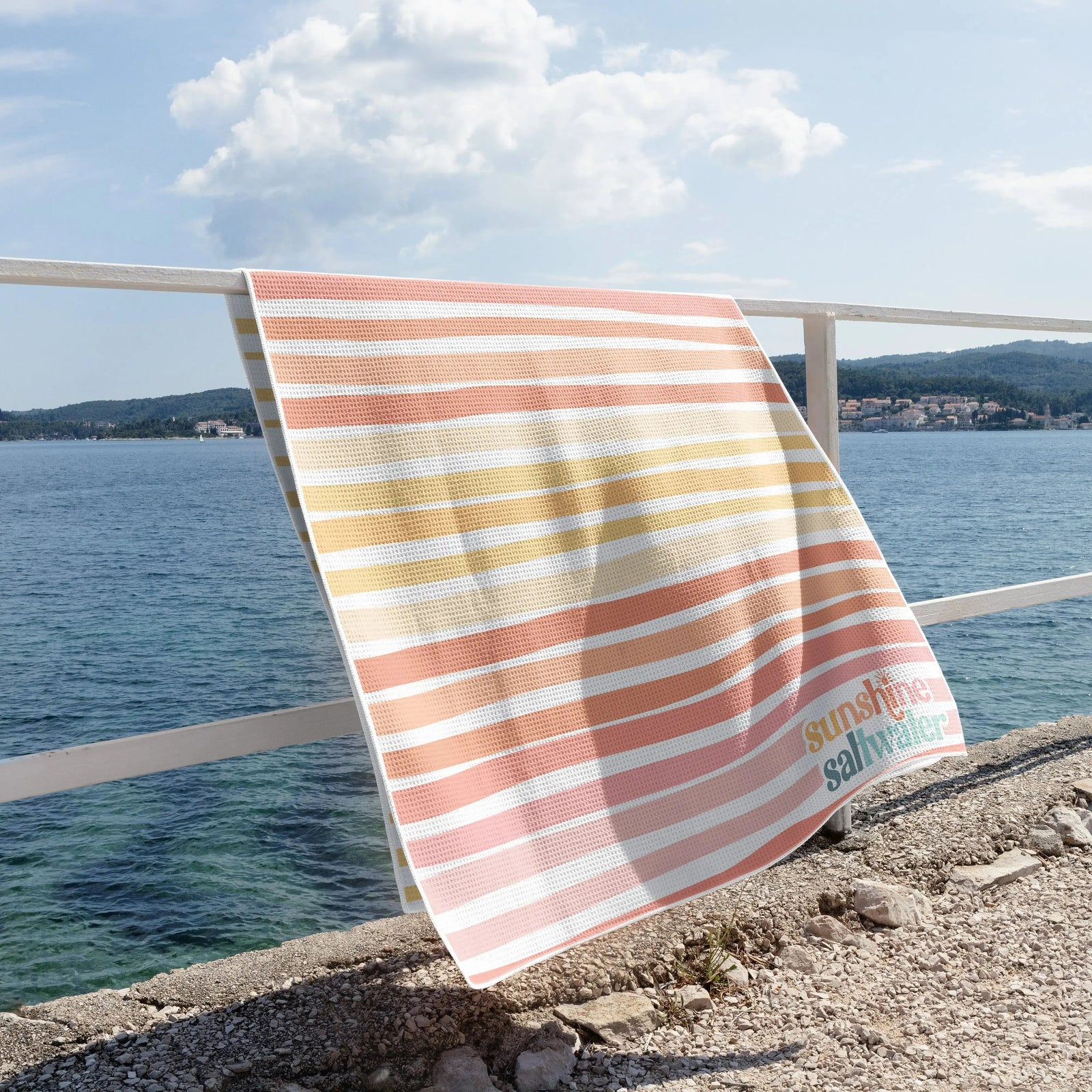 coral and yellow stiped waffle beach towel hanging on railing over the ocean