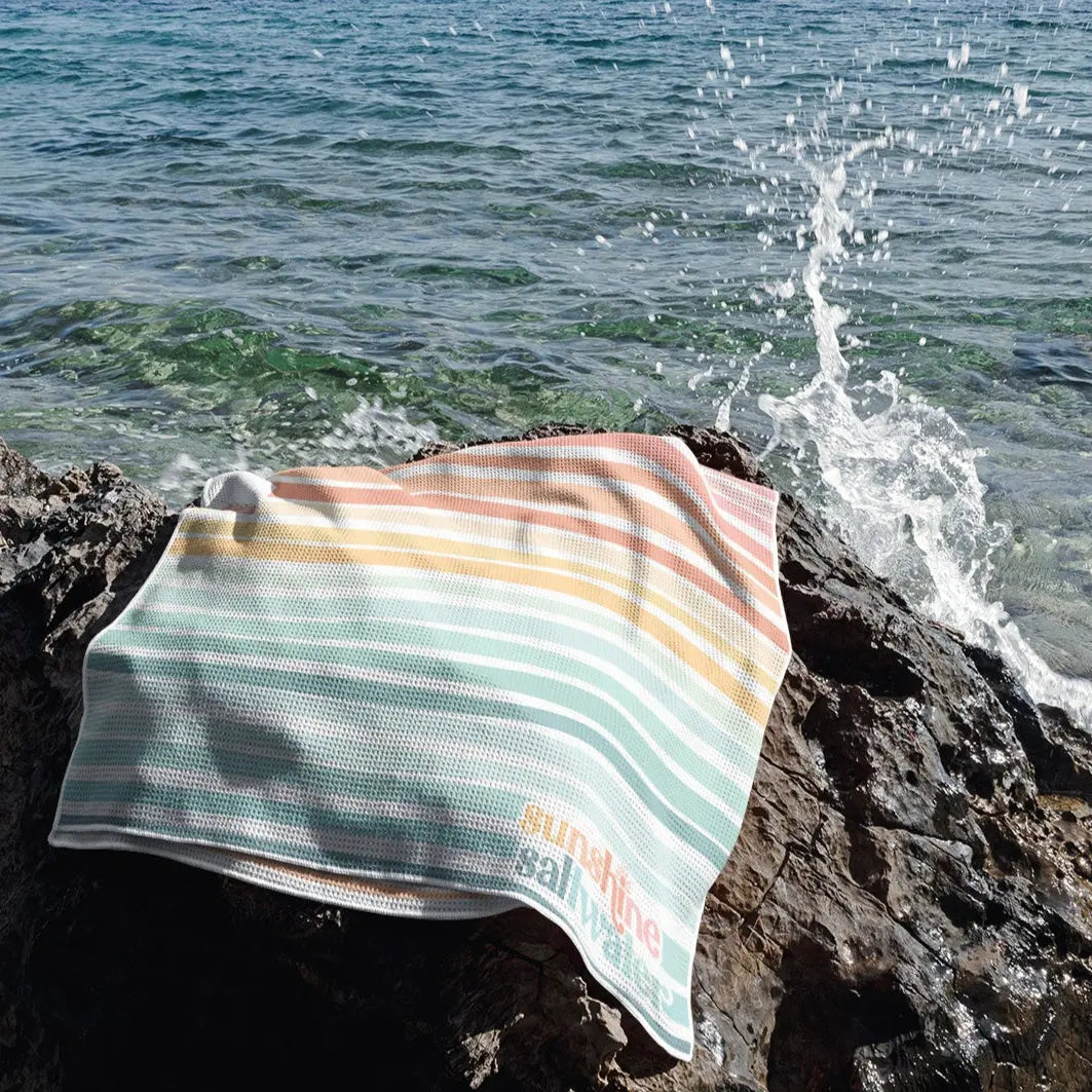 mermaid beach towel in rainbow hues sprawled out on a cliff overlooking ocean