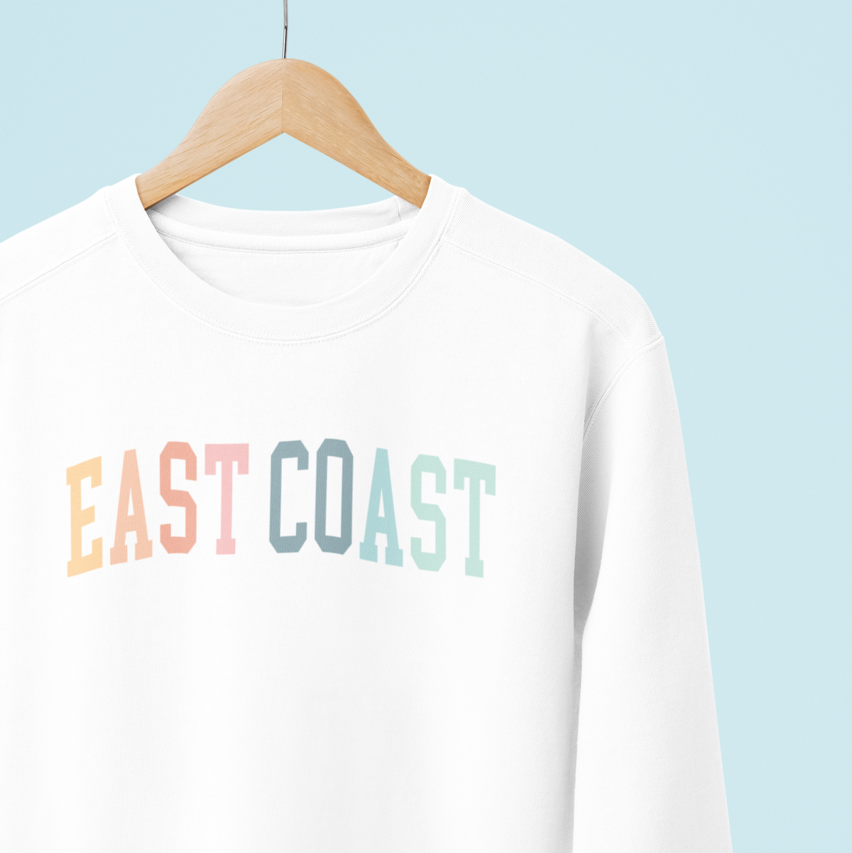 White sweatshirt with &#39;East Coast&#39; text on a hanger against a light blue background