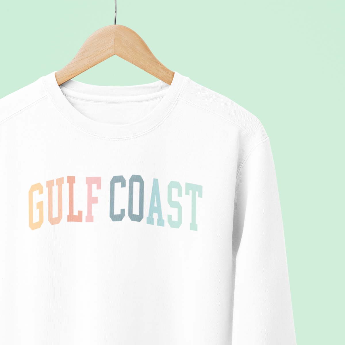 White sweatshirt with &#39;Gulf Coast&#39; text on a hanger against a light green background