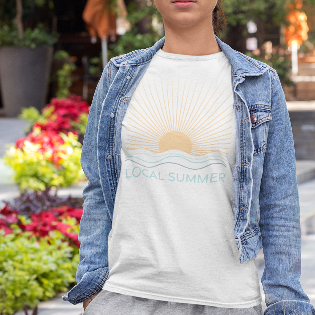 Woman wearing a denim jacket over a white t-shirt with a scenic design, standing outdoors.