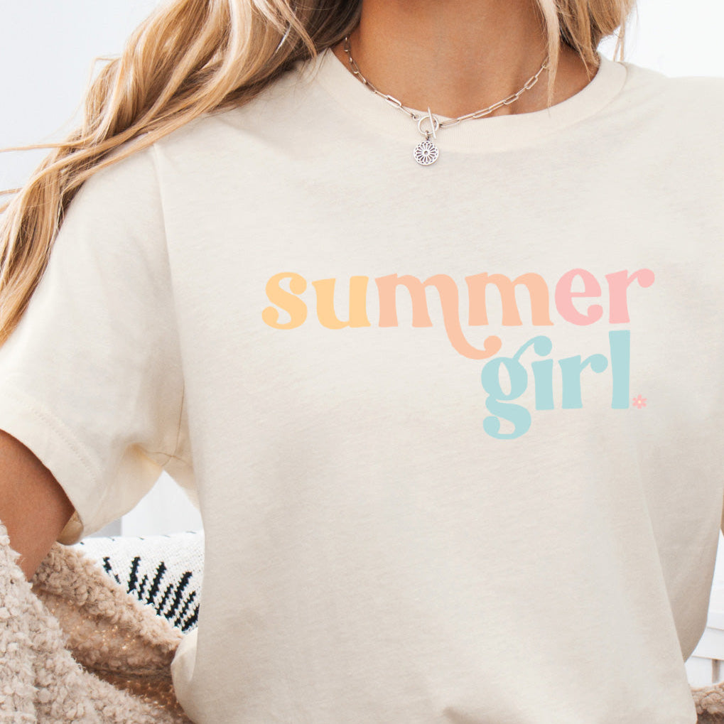 A person wearing a beige t-shirt with the text &#39;summer girl&#39; in multicolored letters.