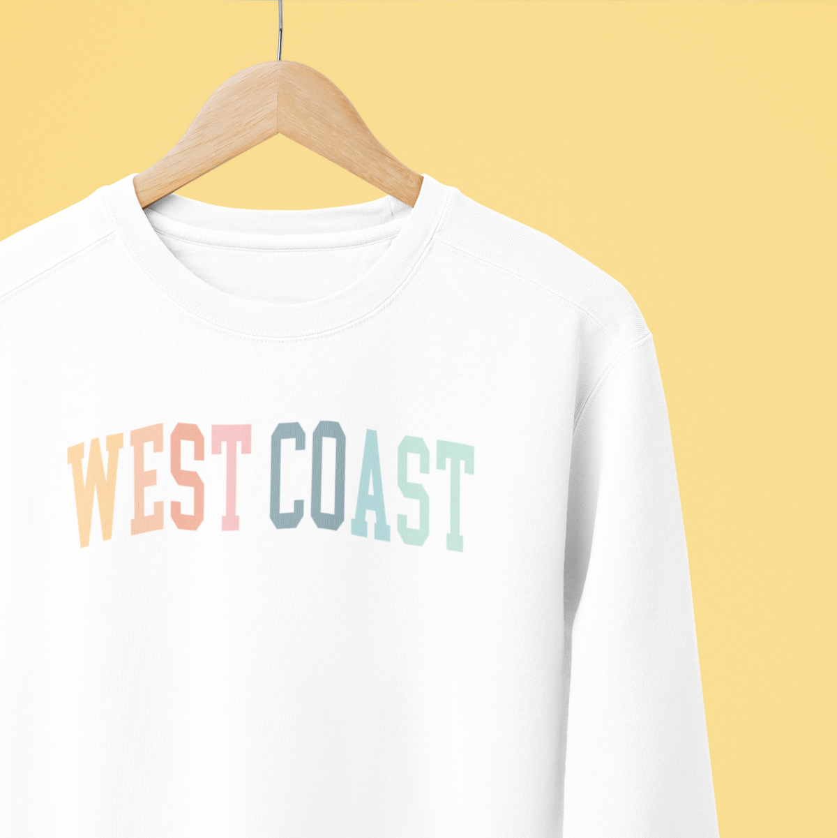 White sweatshirt with &#39;West Coast&#39; text on a hanger against a yellow background